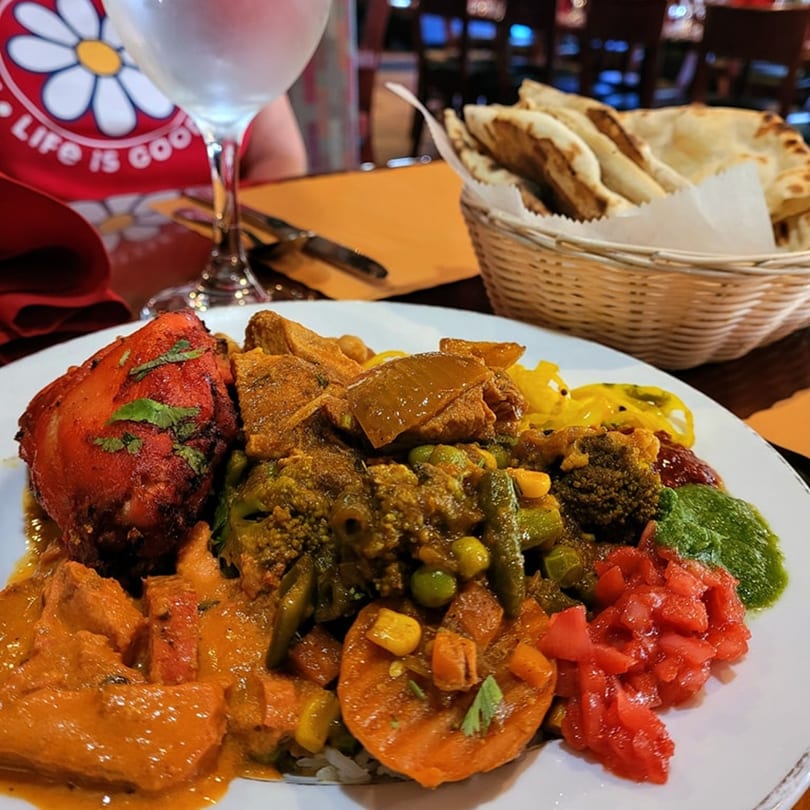 A vibrant Indian platter with tandoori chicken, curries, vegetables, and chutneys, with naan in a basket.